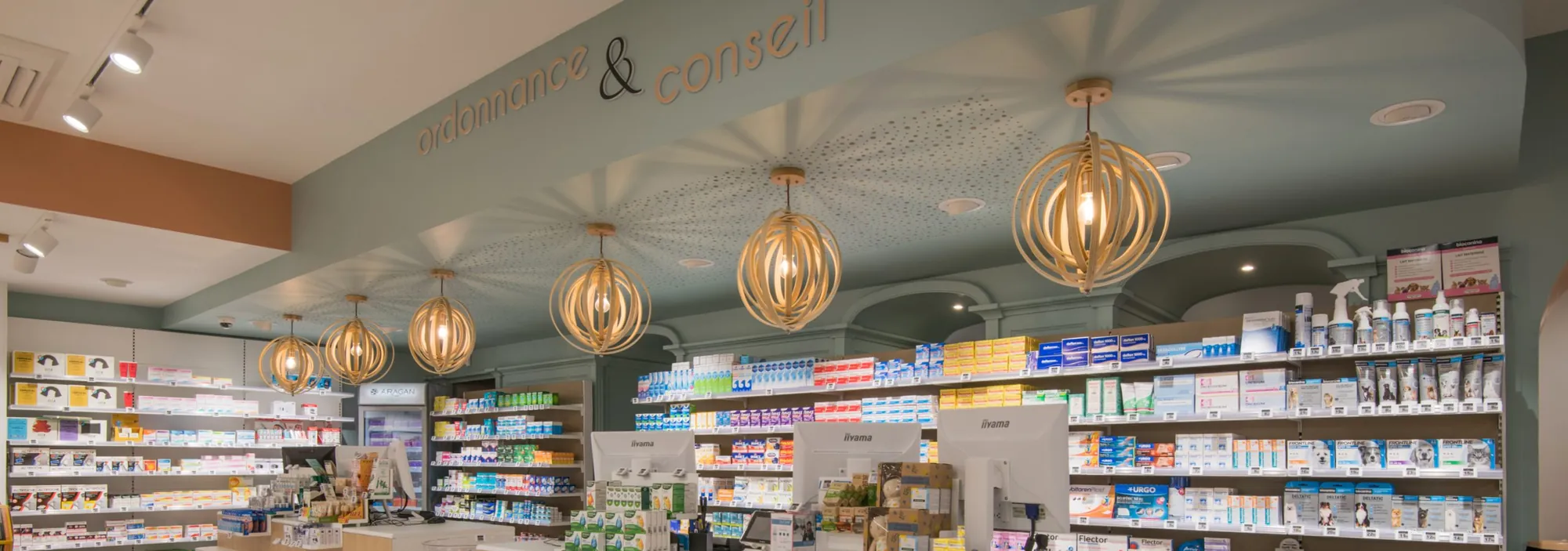 Comptoir d’une officine : espace ordonnance et conseil, rayonnages et suspensions en bois.